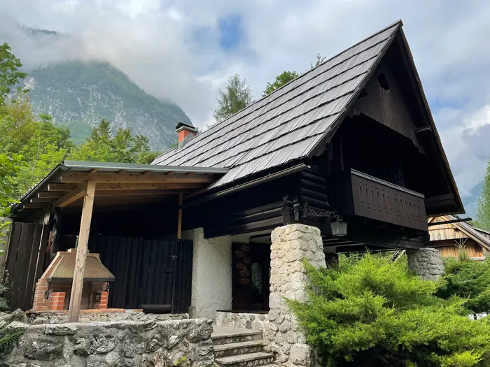 Stranski del Koče pri Rdeči Bukvi s pokritim zunanjim žarom in temno leseno fasado