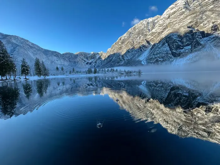Zimski pogled na Bohinjsko jezero z gorami, ki se zrcalijo v mirni vodi